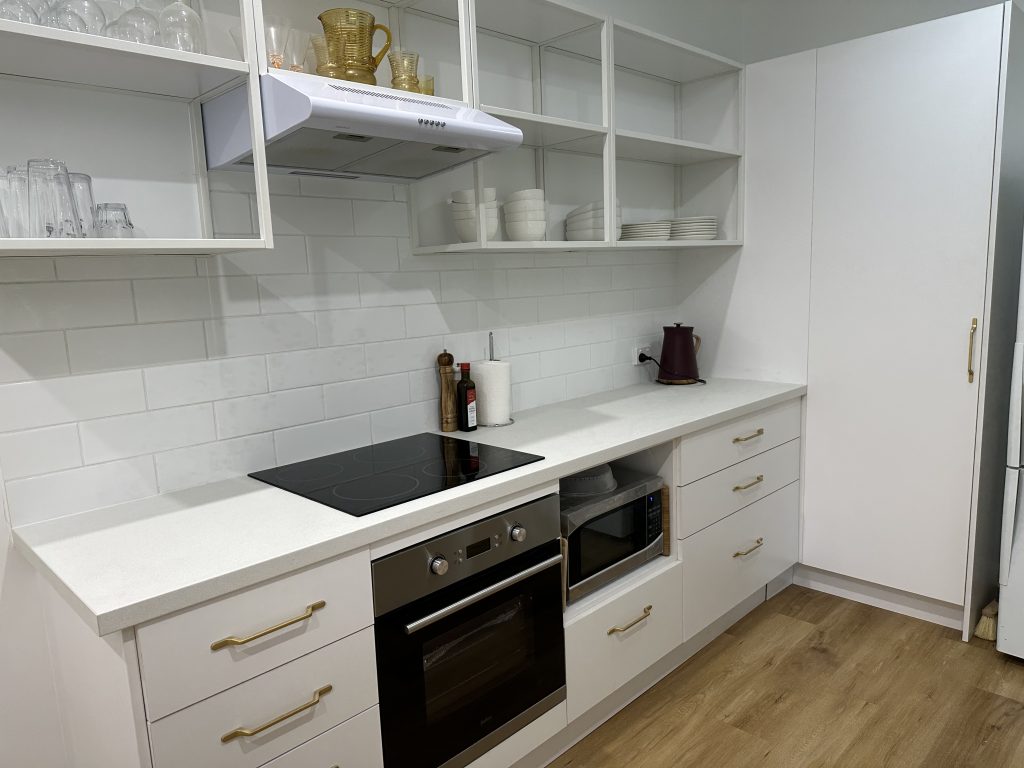 A clean, modern kitchen area with white cabinetry, white countertops, and white subway tile backsplash.