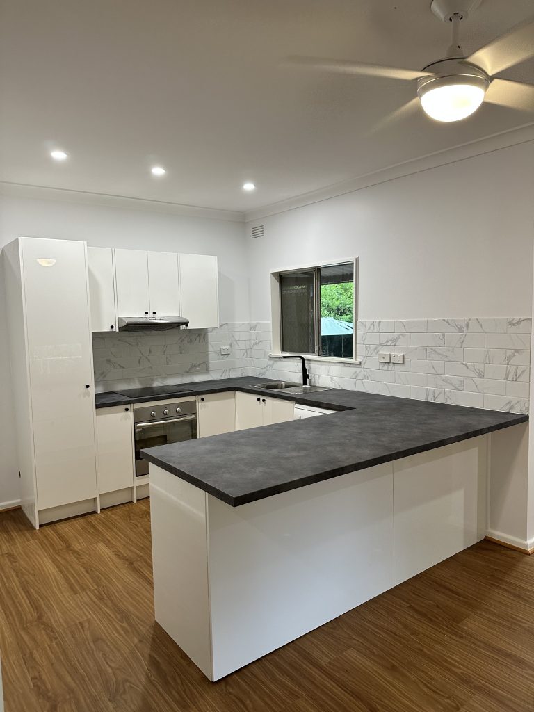 A newly renovated, modern kitchen featuring white high-gloss cabinets and a contrasting dark grey U-shaped laminate countertop.