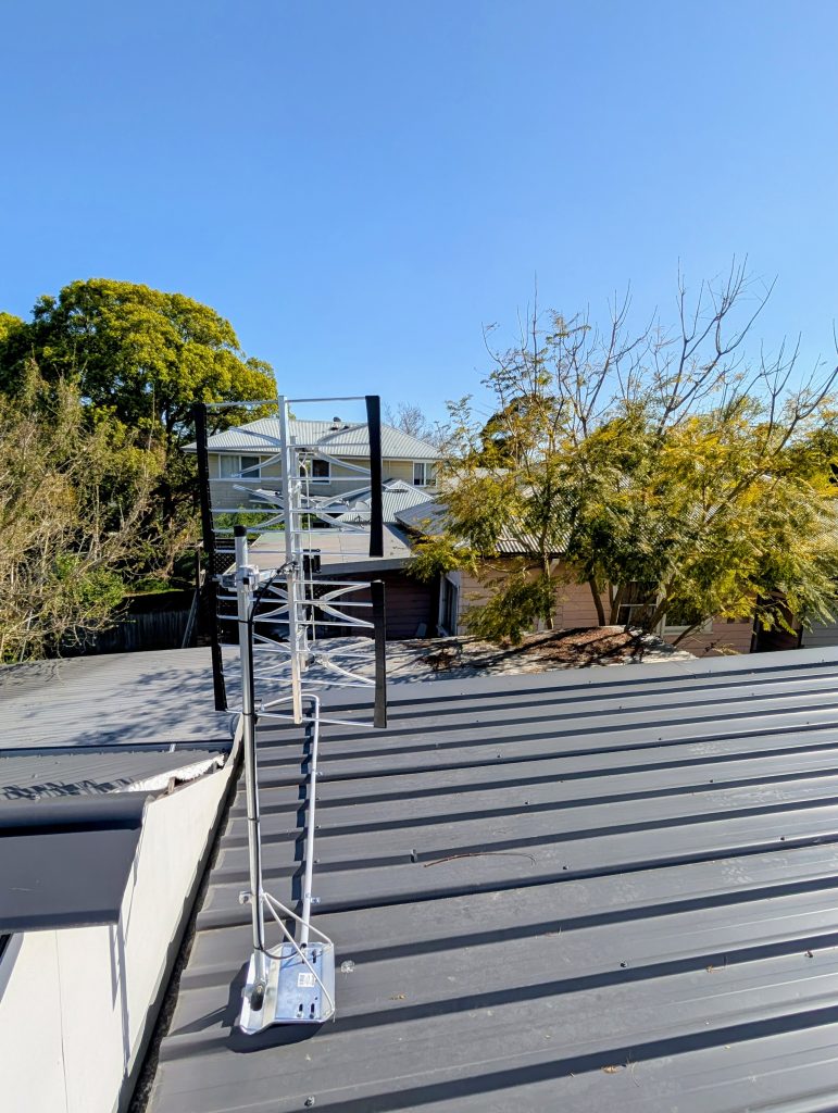 A residential rooftop view featuring a shiny, white, horizontally-polarised Yagi antenna mounted on a grey corrugated metal roof.