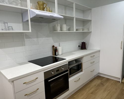 A clean, modern kitchen area with white cabinetry, white countertops, and white subway tile backsplash.
