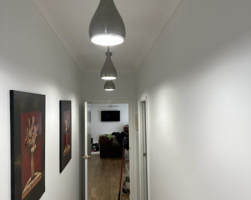 A long, white hallway illuminated by a series of four vertically aligned, contemporary, teardrop-shaped pendant lights hanging from the ceiling.