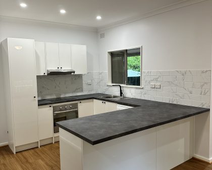 A newly renovated, modern kitchen featuring white high-gloss cabinets and a contrasting dark grey U-shaped laminate countertop.