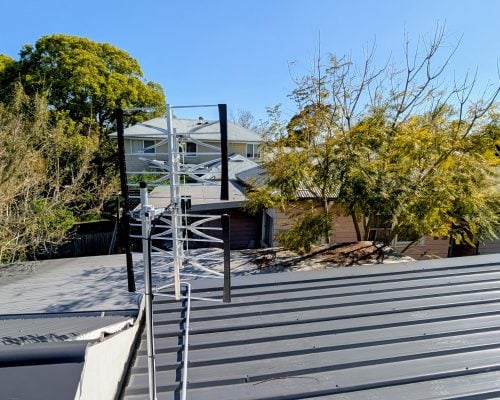A residential rooftop view featuring a shiny, white, horizontally-polarised Yagi antenna mounted on a grey corrugated metal roof.