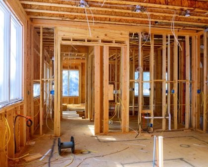 worker installs electrical wires, insulation, and ceiling light before plasterboard in new house