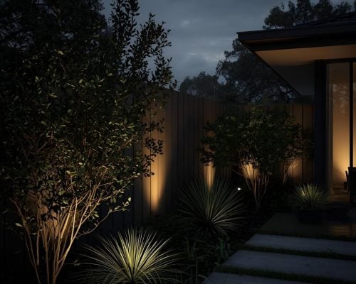 A contemporary garden and patio area, dramatically illuminated by landscape lighting.