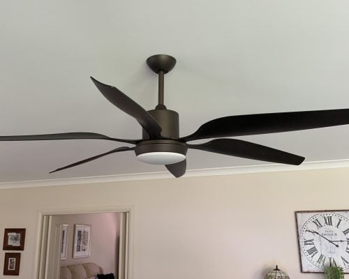 A modern ceiling fan with five long, dark brown or black curved blades is mounted on a white ceiling.