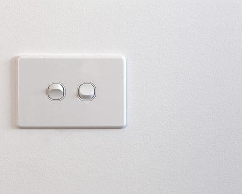 A modern, rectangular, white double light switch mounted on a plain white wall.