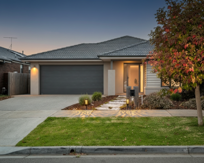 House features a grey tiled roof, light beige walls, and a large, dark grey double garage door.